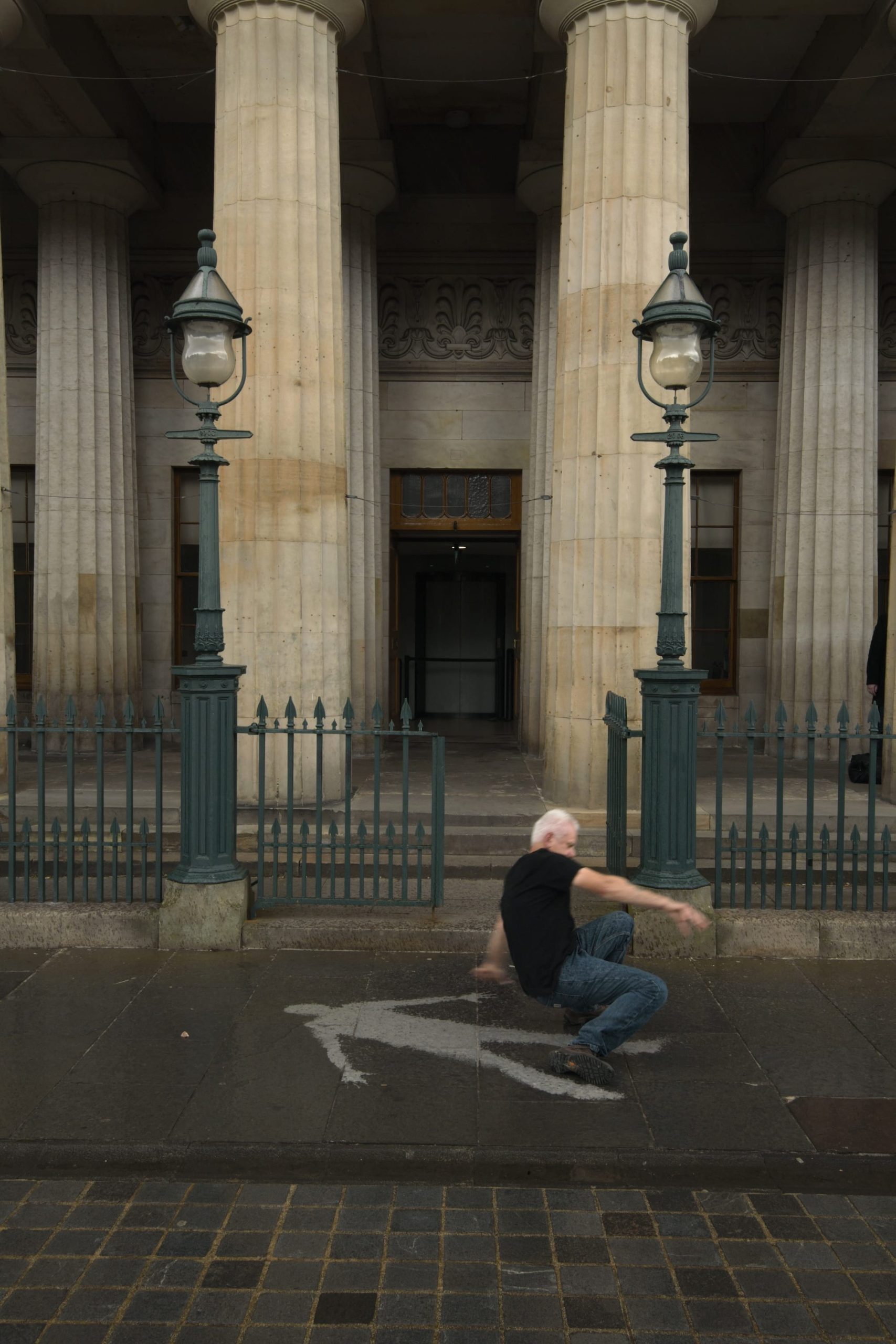a photograph of artist Andy Goldsworthy creating a temporary art installation outside of the Scottish Royal Academy, laying on the pavement in the rain so that when he stood up, his impression on the sidewalk was dry