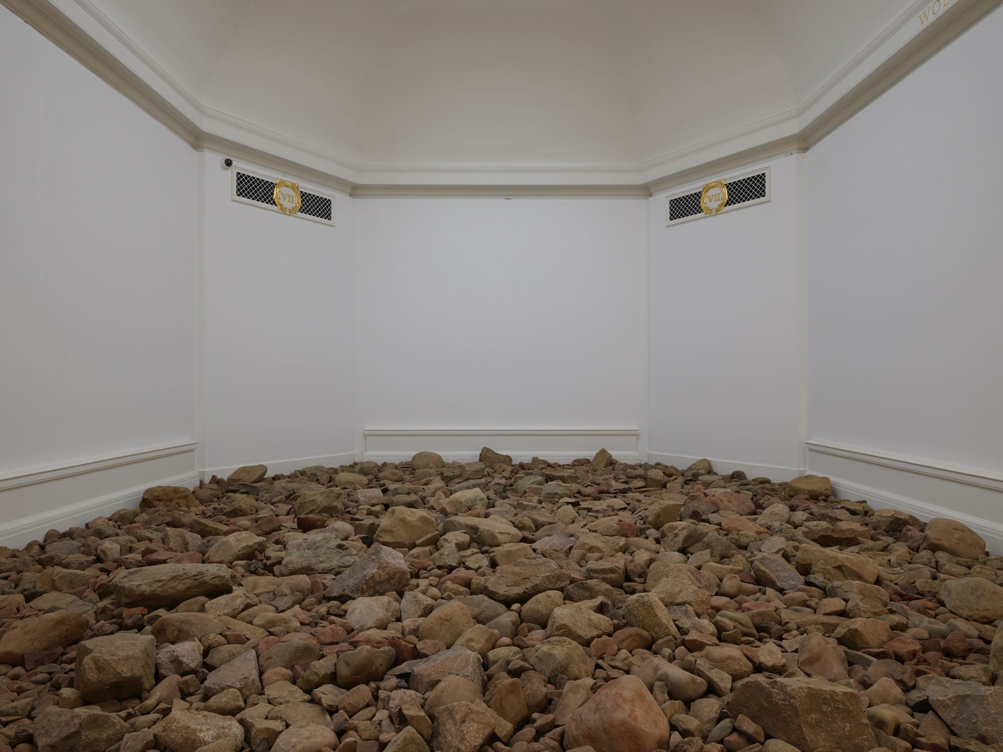 an installation view of 'Andy Goldsworthy: Fifty Years' at National Galleries of Scotland, featuring a floor covered in brown stones