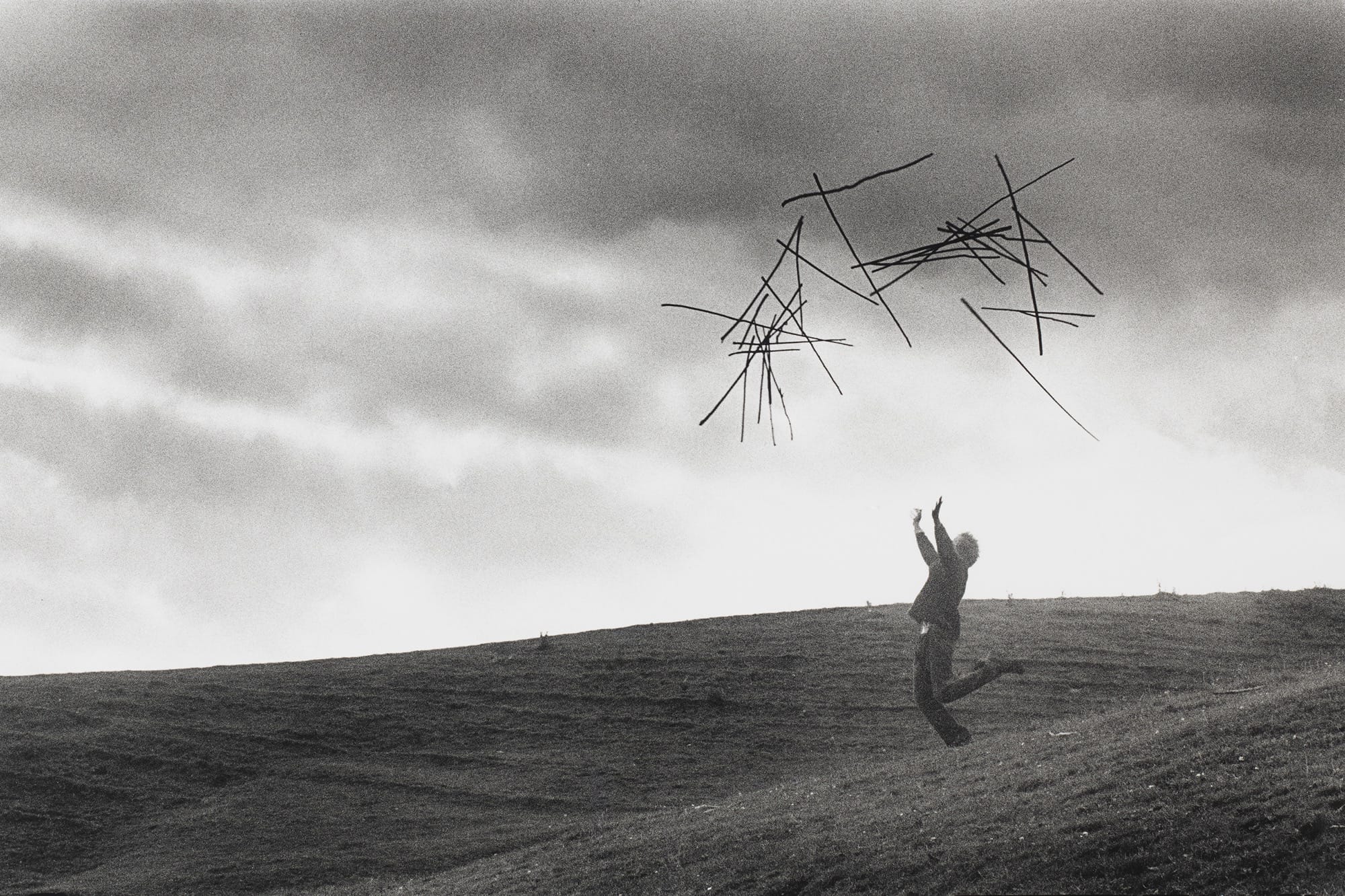 a photograph by Andy Goldsworthy showing the artist throwing hazel sticks in the air