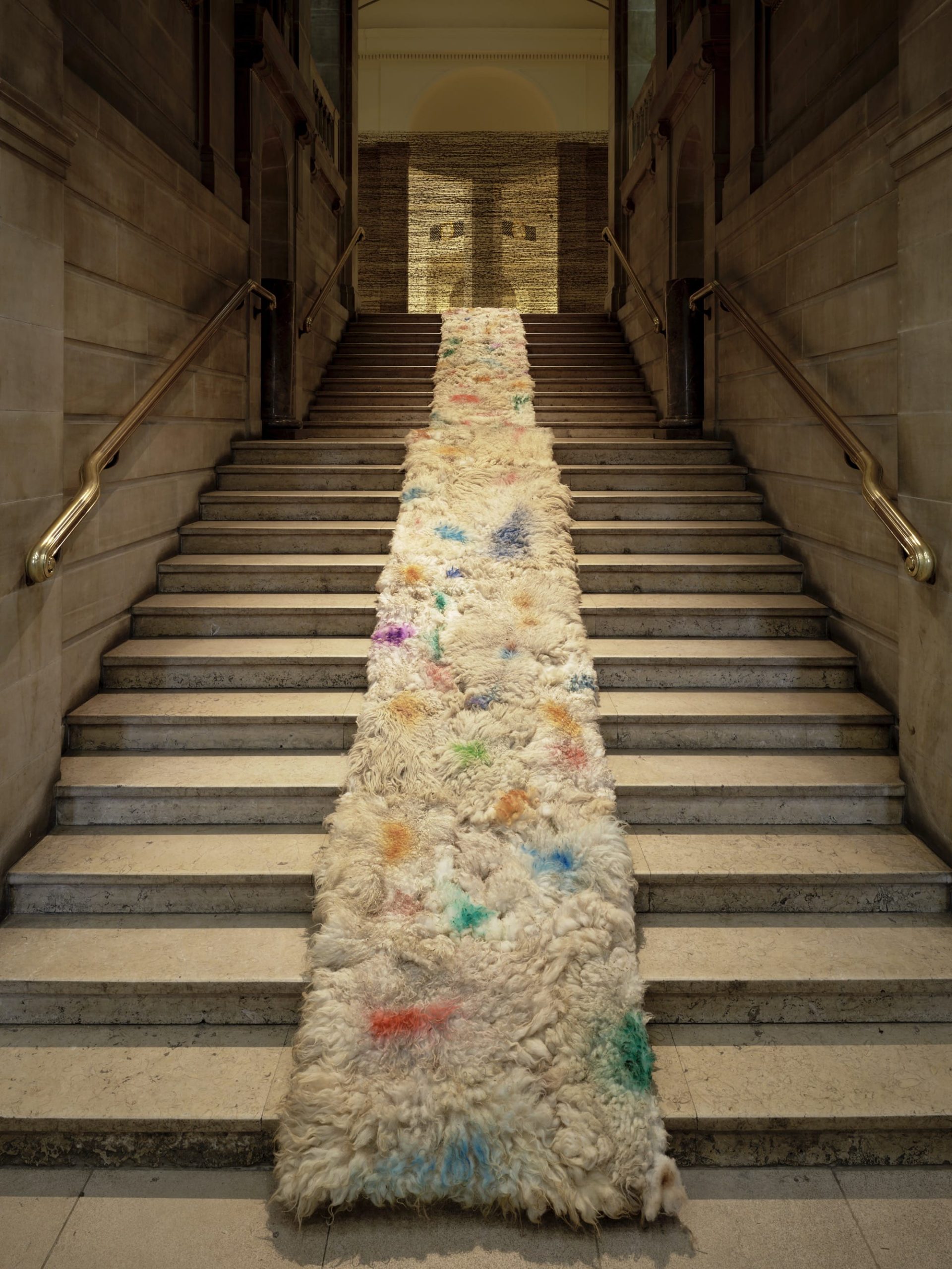 an installation view of 'Andy Goldsworthy: Fifty Years' at National Galleries of Scotland, featuring a large wool runner sculpture down a long staircase