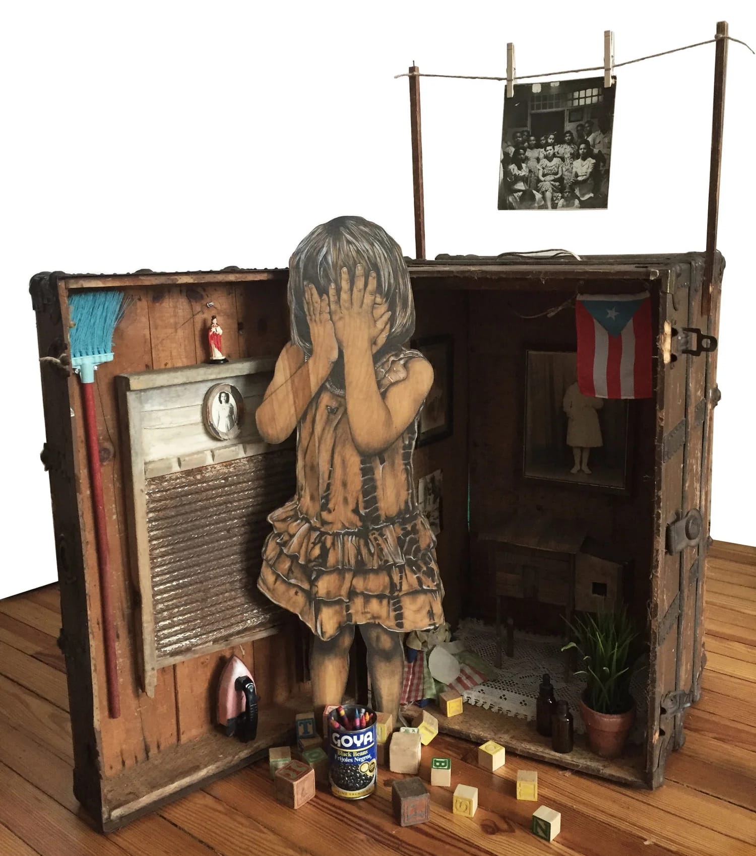 an open trunk with a portrait of a child with her hands over her eyes. a washboard is behind her and blocks at her feet