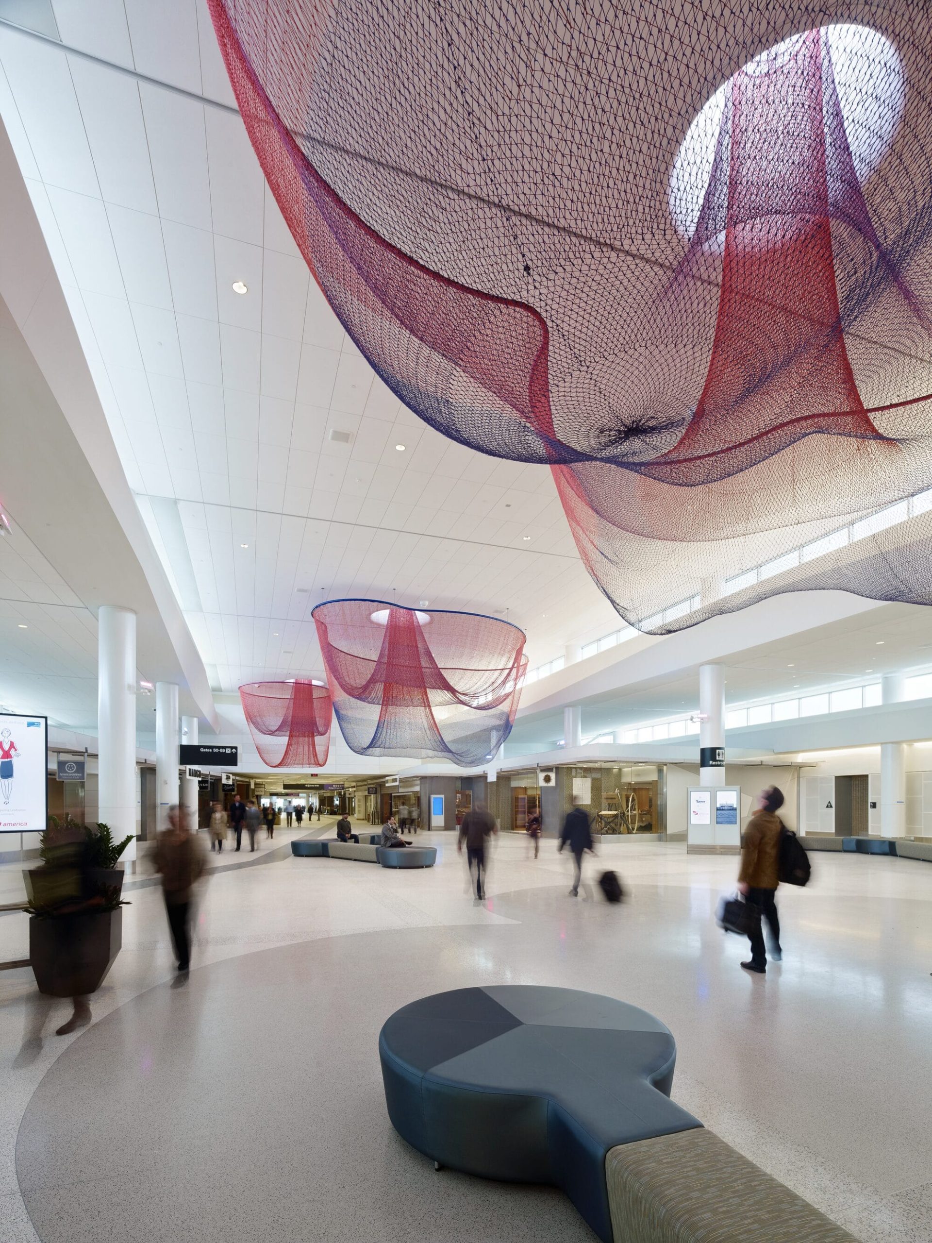 people walk underneath a pink Janet Echelman installation suspended from the ceiling