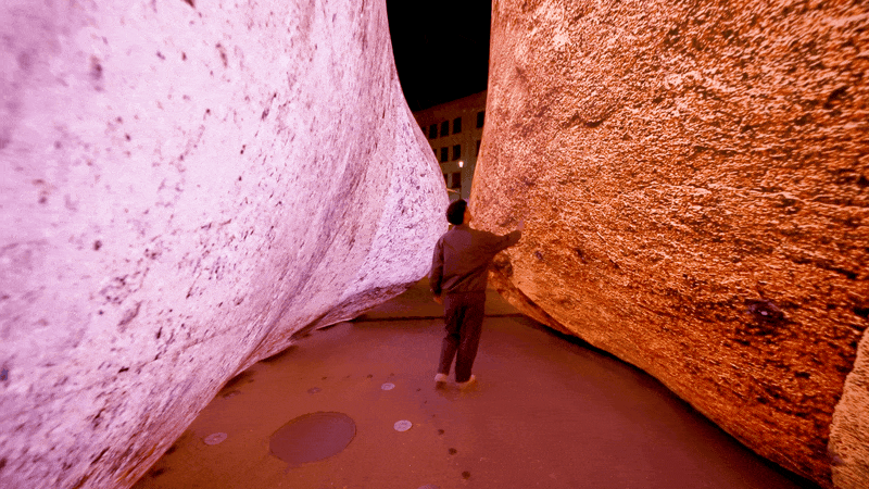 a gif of a person walking between a pink and orange inflatable