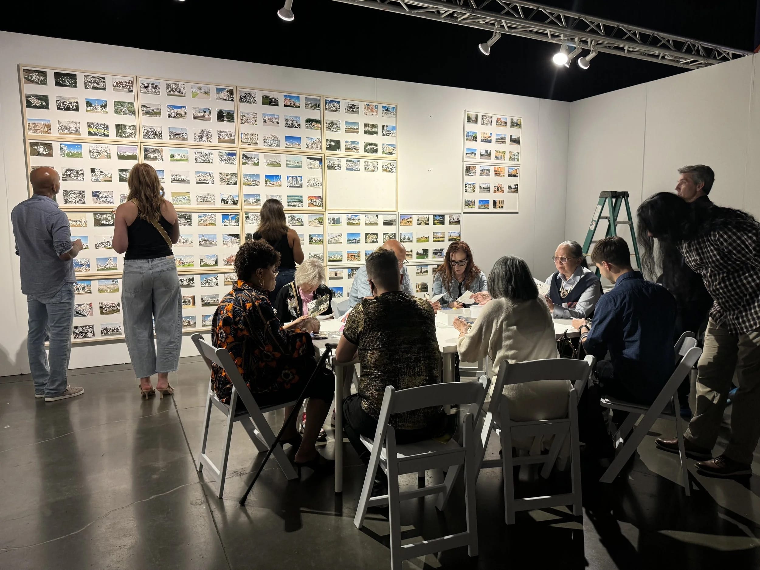 a group of people at a table working with small postcard size images on the wall behind them