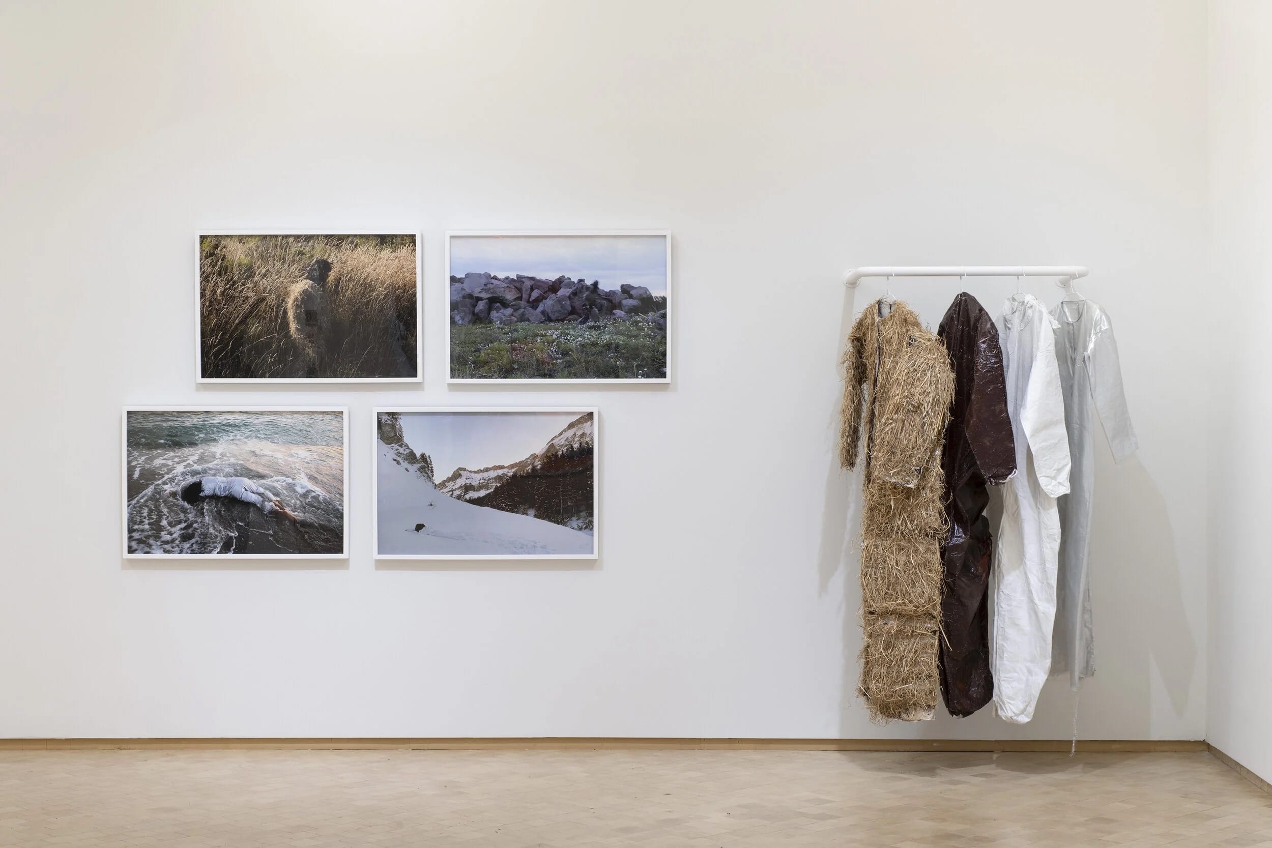 four suits hanging on a rack with four images framed on a gallery wall