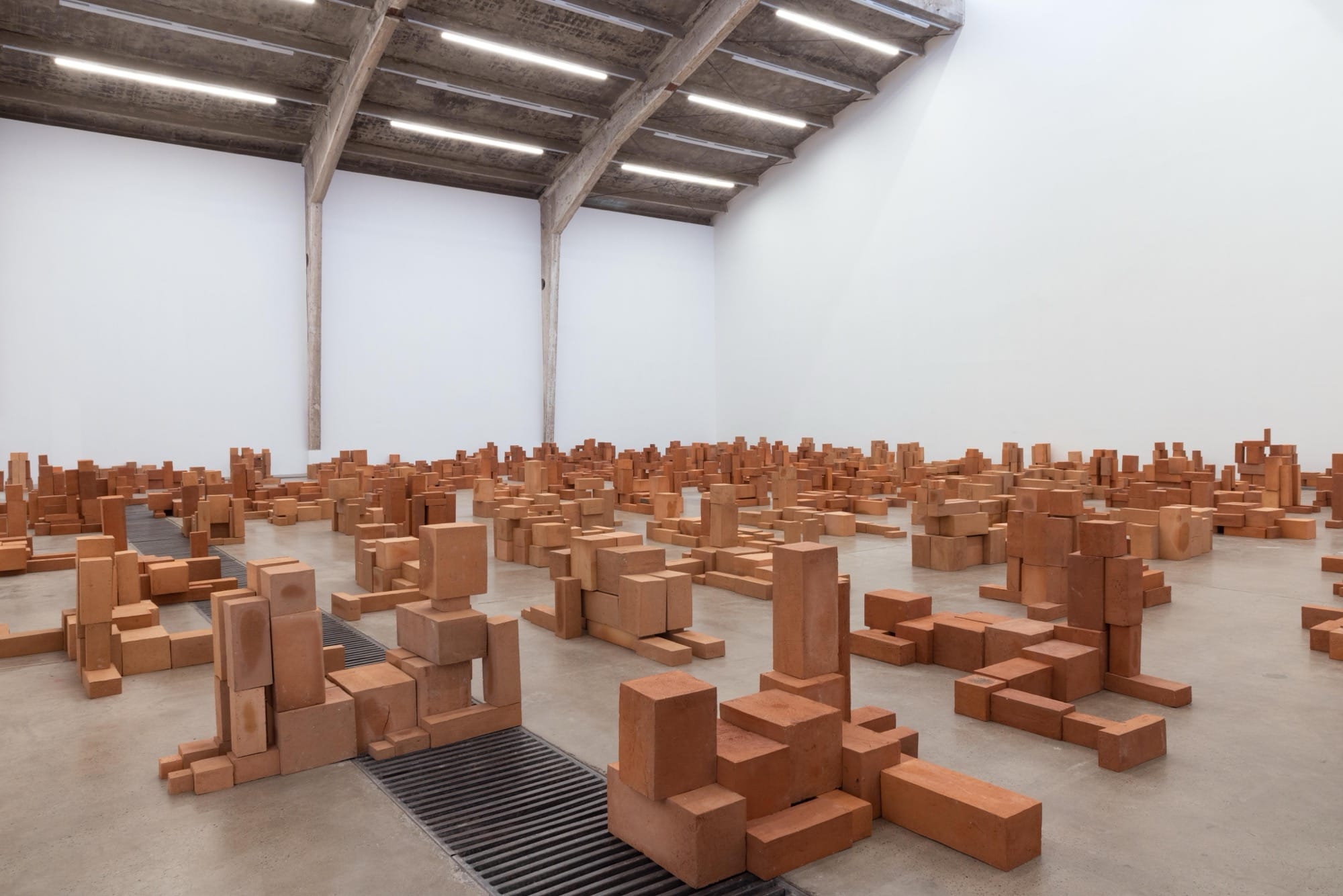 a detail of a room-size art installation by Antony Gormley of blocky terracotta forms resembling human figures in various positions