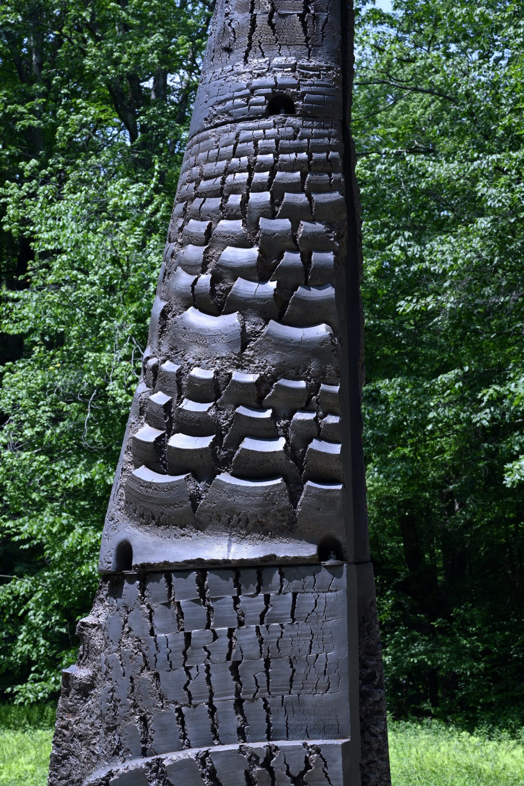 a detail of a conical, textured, black, abstract sculpture by Yō Akiyama installed outdoors