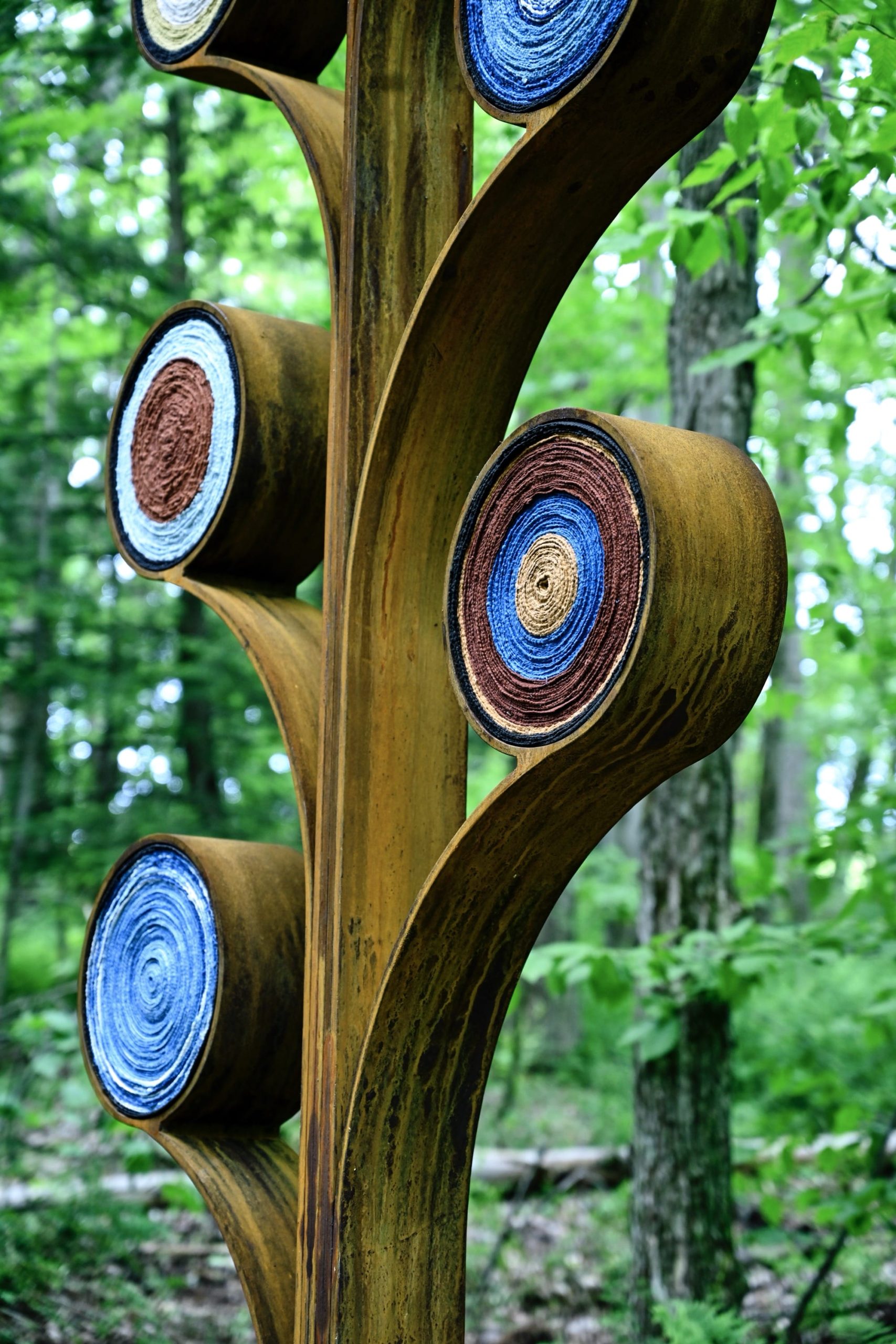 a detail of two abstract tree forms installed in a wooded area, by artist Aboubakar Fofana, with dyed fiber elements