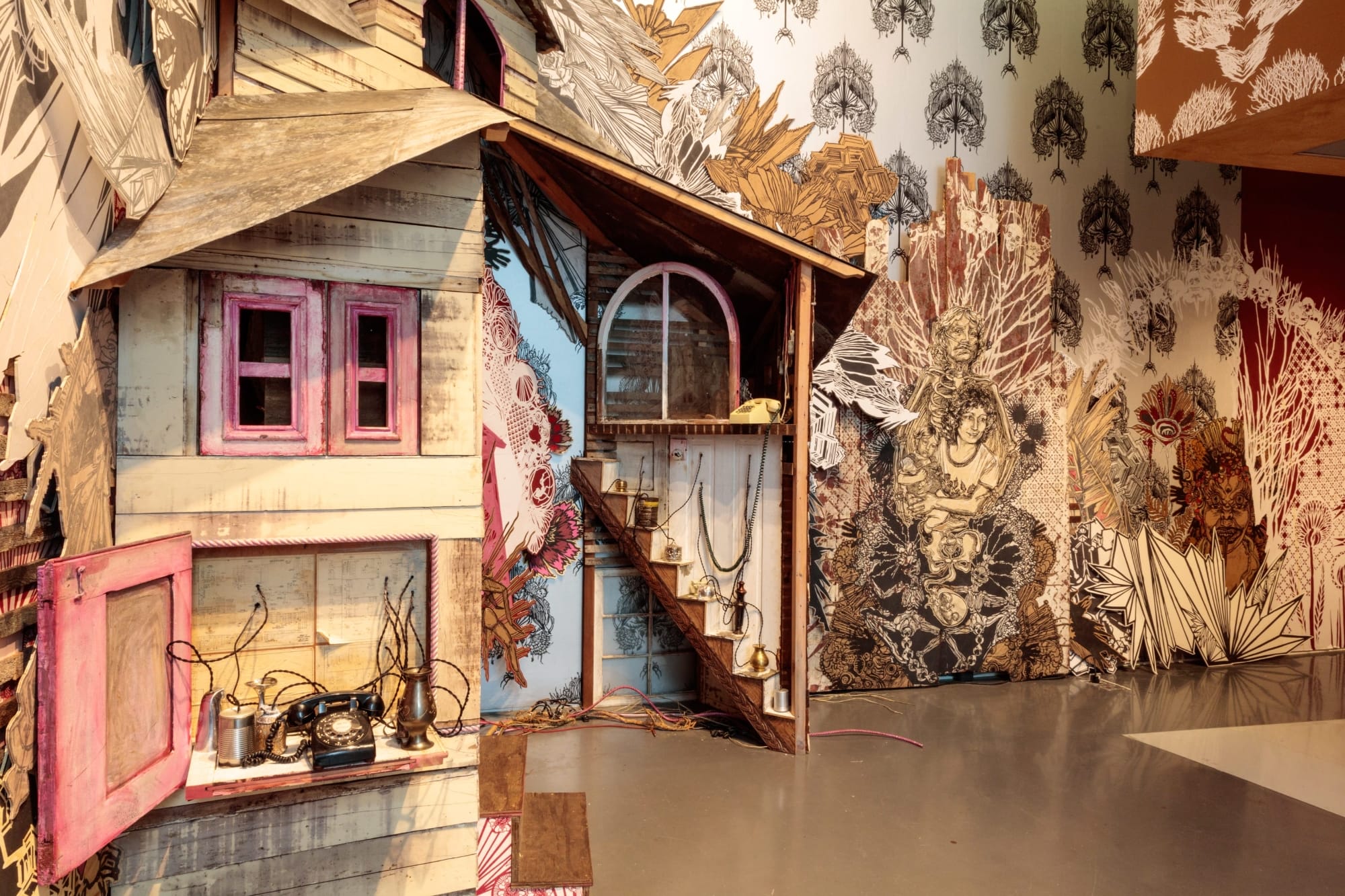 an installation with patterned wallpaper, figures, vignettes, and a tarantula woman at the center