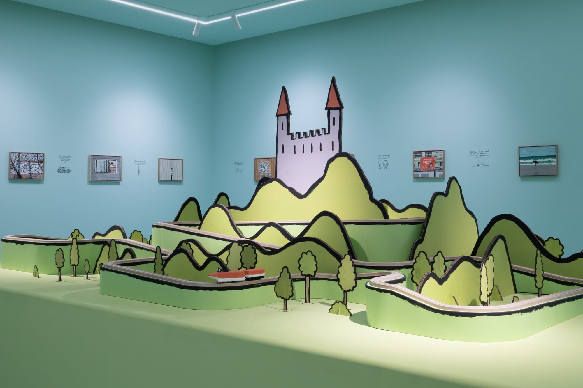 a sculptural castle sits behind green grass in a blue gallery