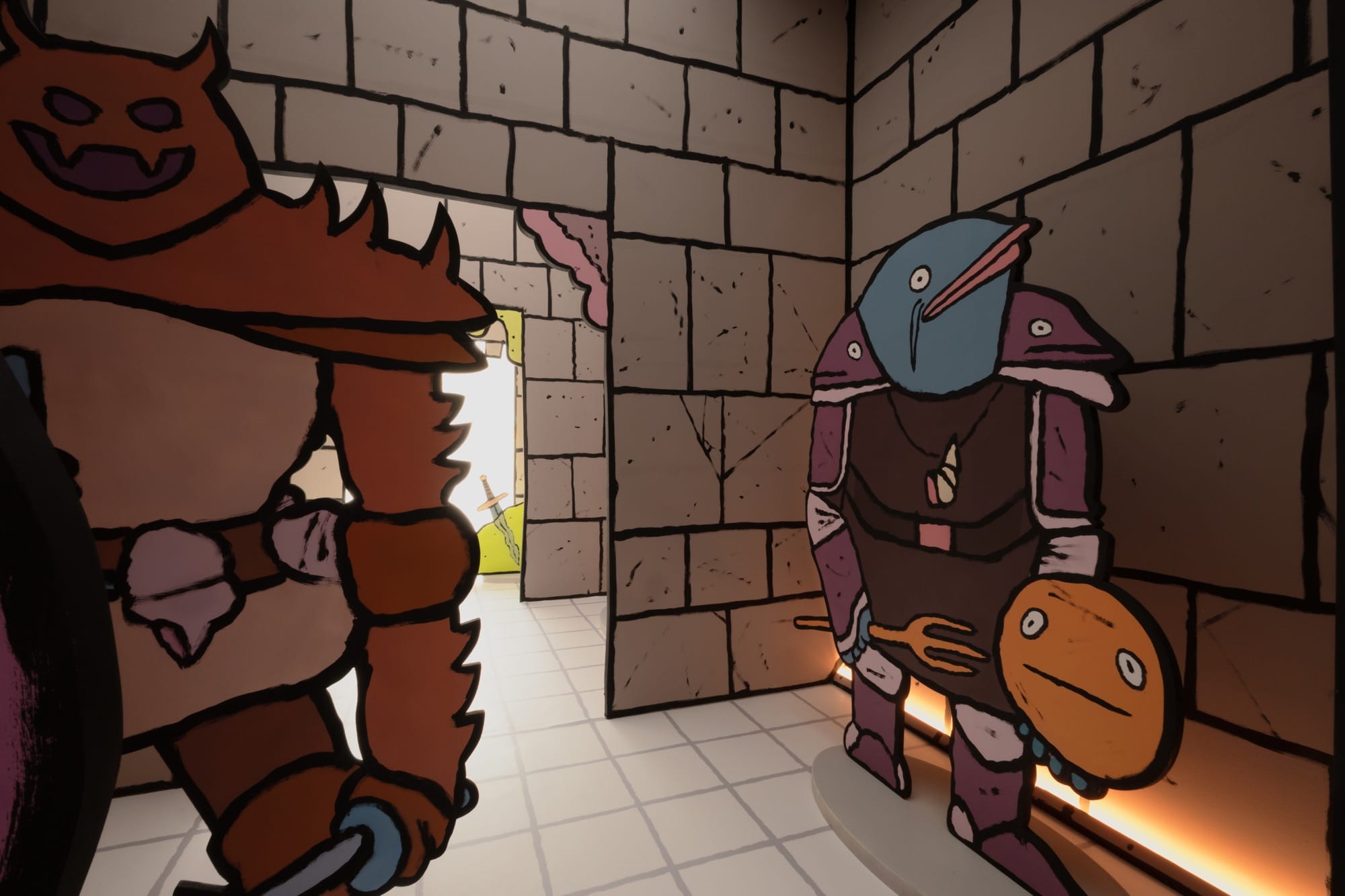 two cartoonish sculptures, one with a monstrous suit and the other with several fish heads, stands in a small room