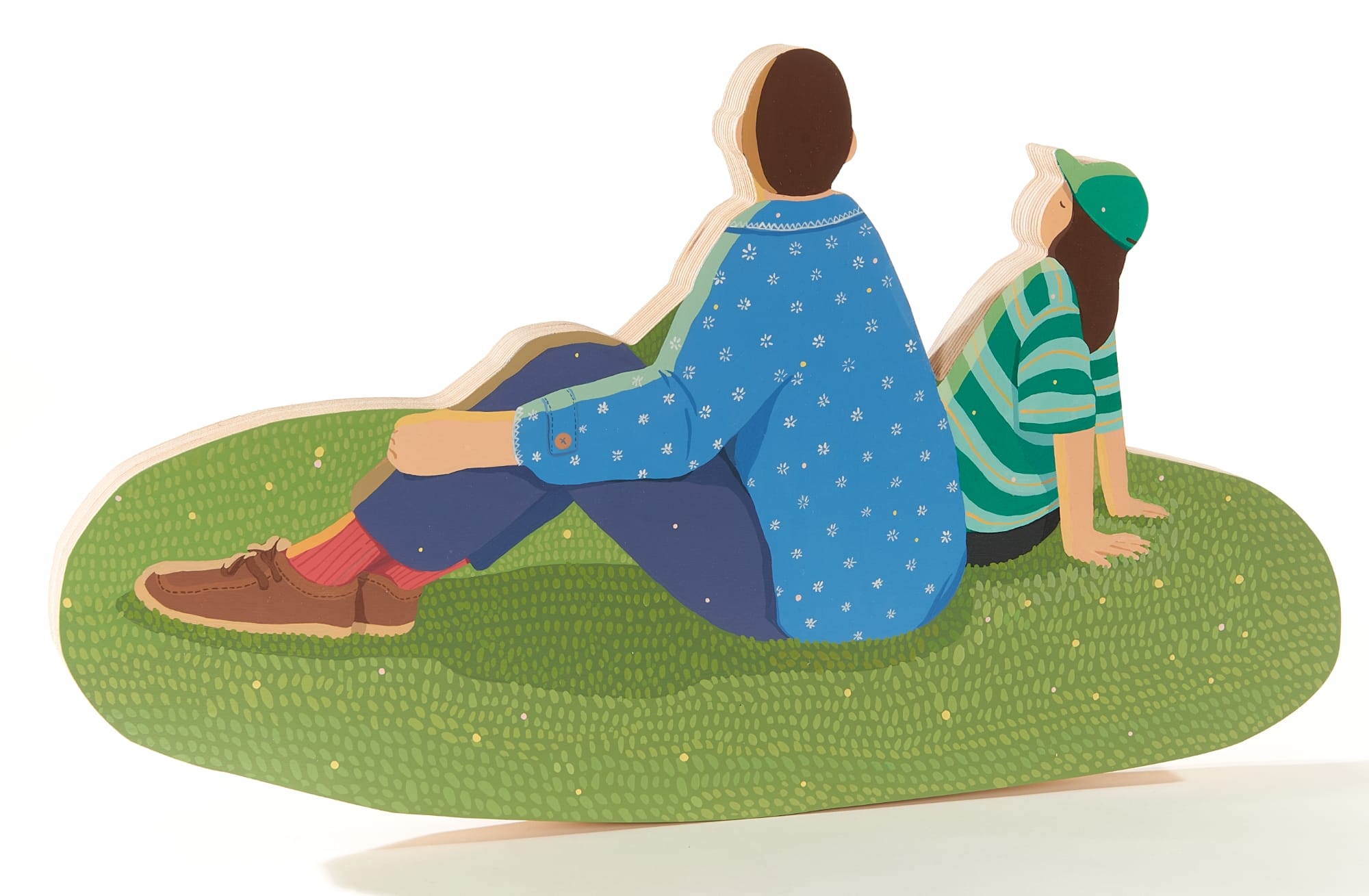 a wood sculpture of two people who are lounging on the grass