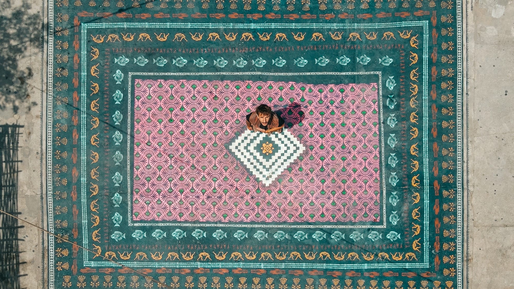 a drone shot of artist Mateo standing on his spray-painted ornate carpet on a rooftop in Dakar