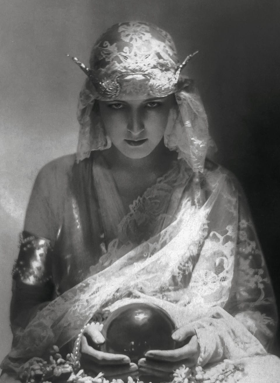 a black-and-white photograph of a woman in elaborate 1920s dress, holding a crystal ball