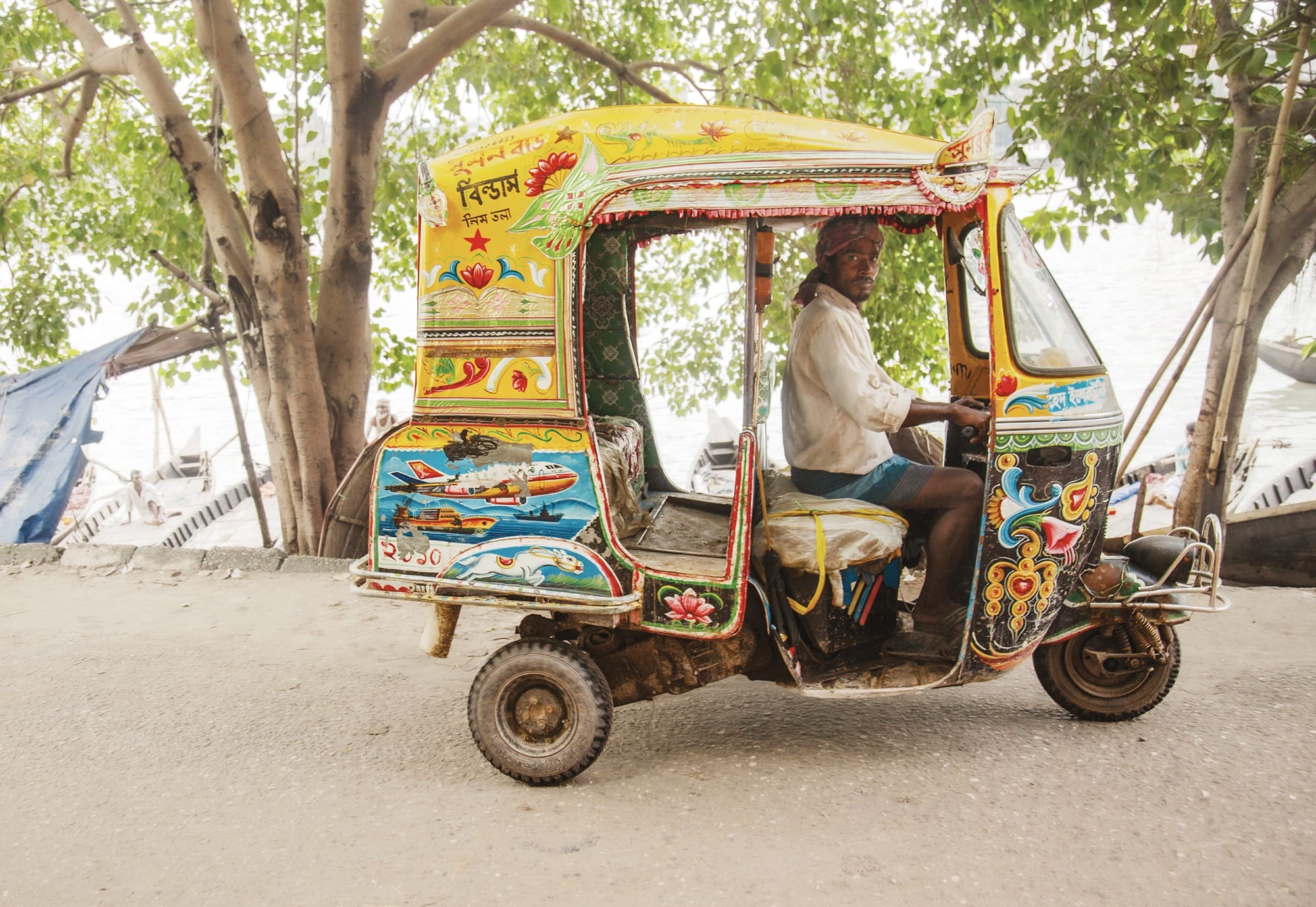 a person drives a small, elaborately painted yellow tuk