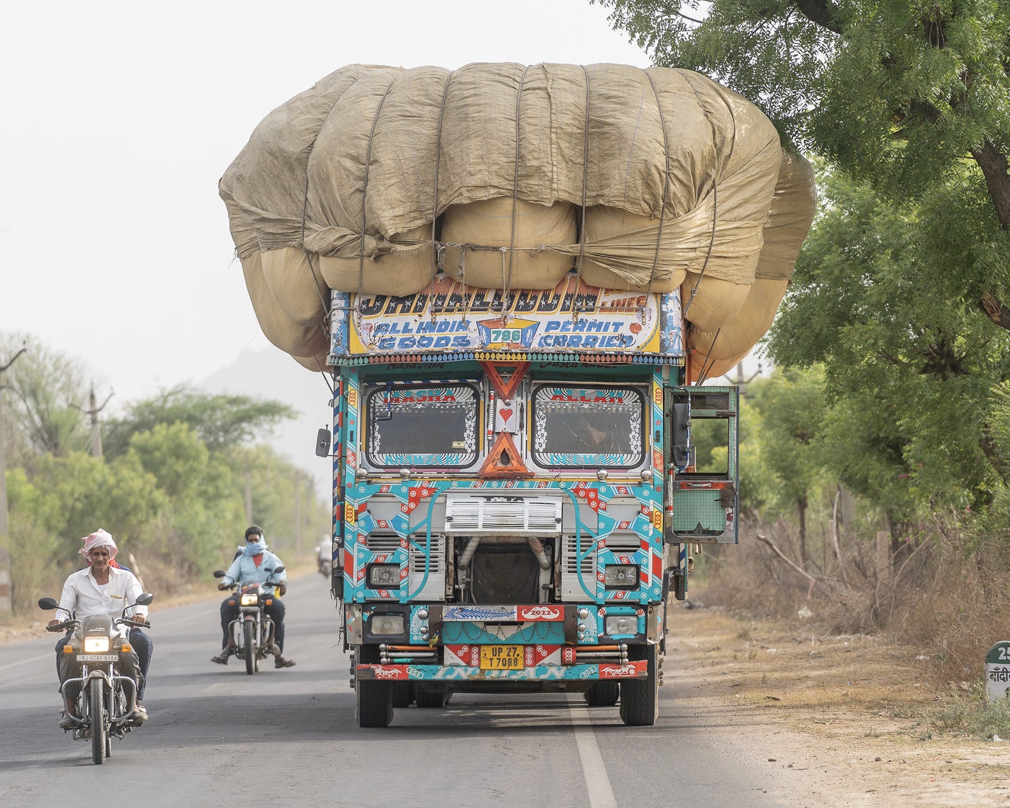 a colorfully painted truck hauling a massive, puffy load with two motorcylists on the road next to