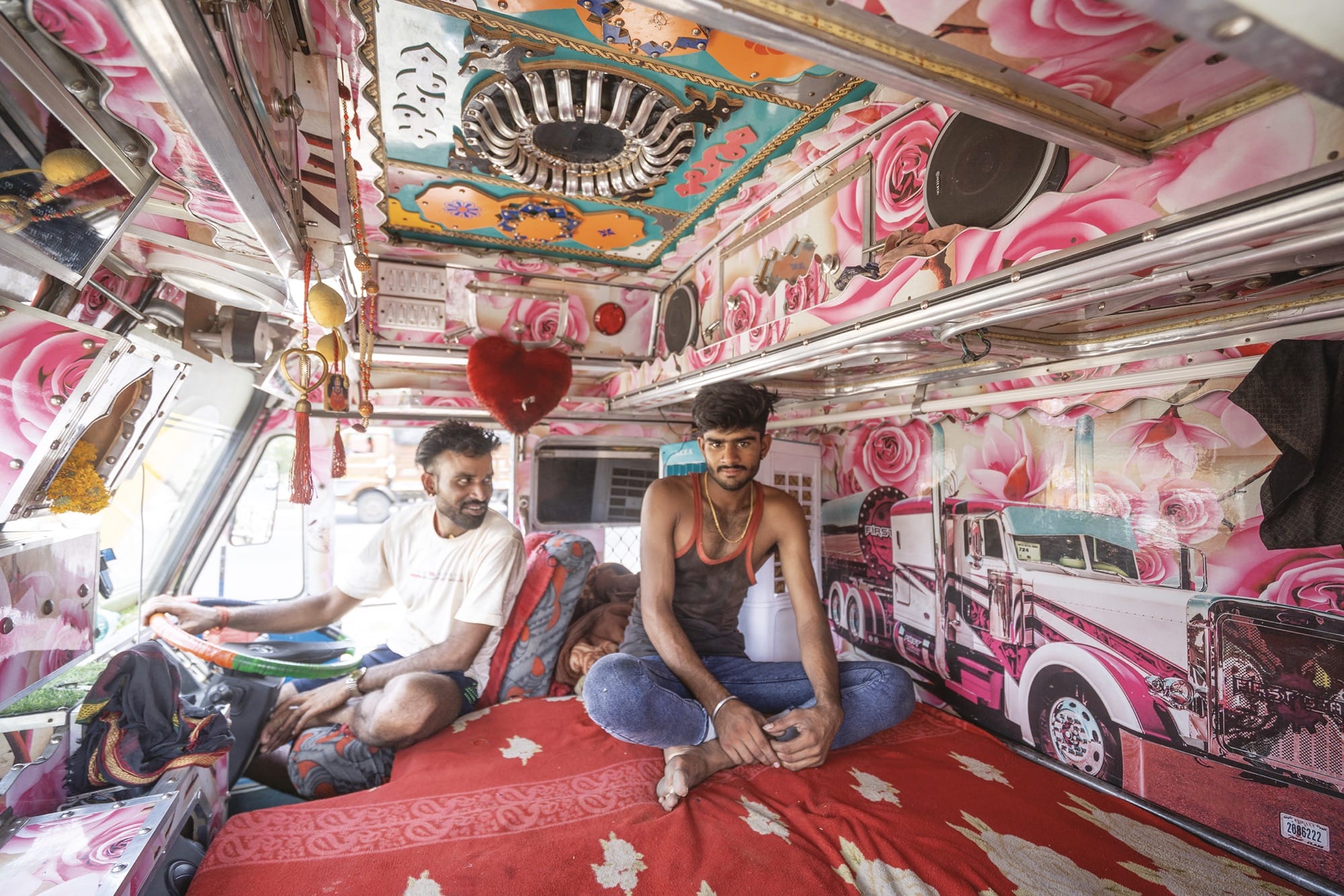 two men sit inside the cab of a truck that's painted with bright motifs