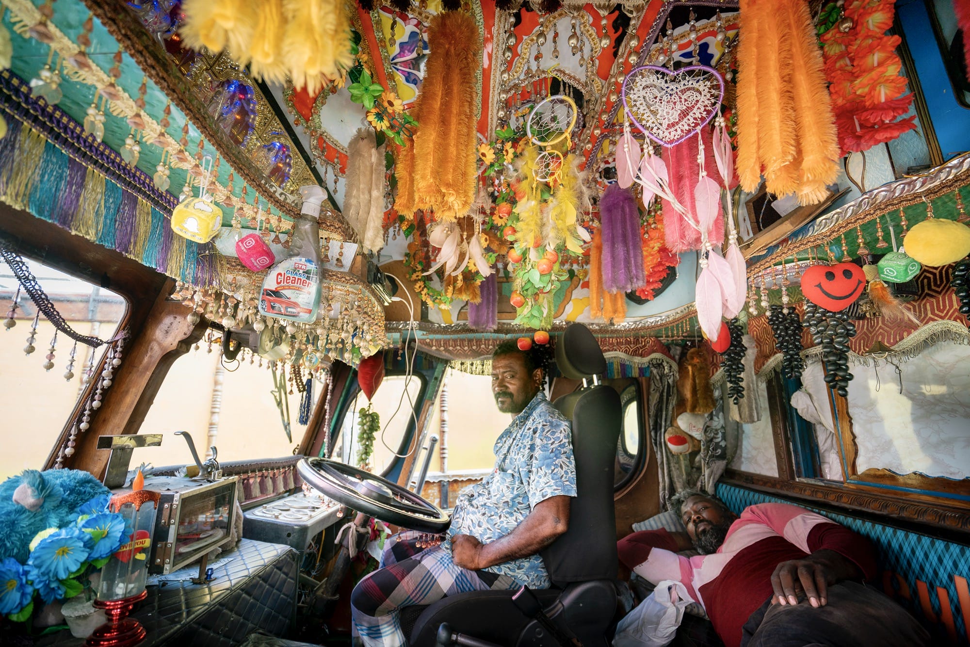 a person at the wheel of a truck with dangling fringe and other vibrant objects on the ceiling