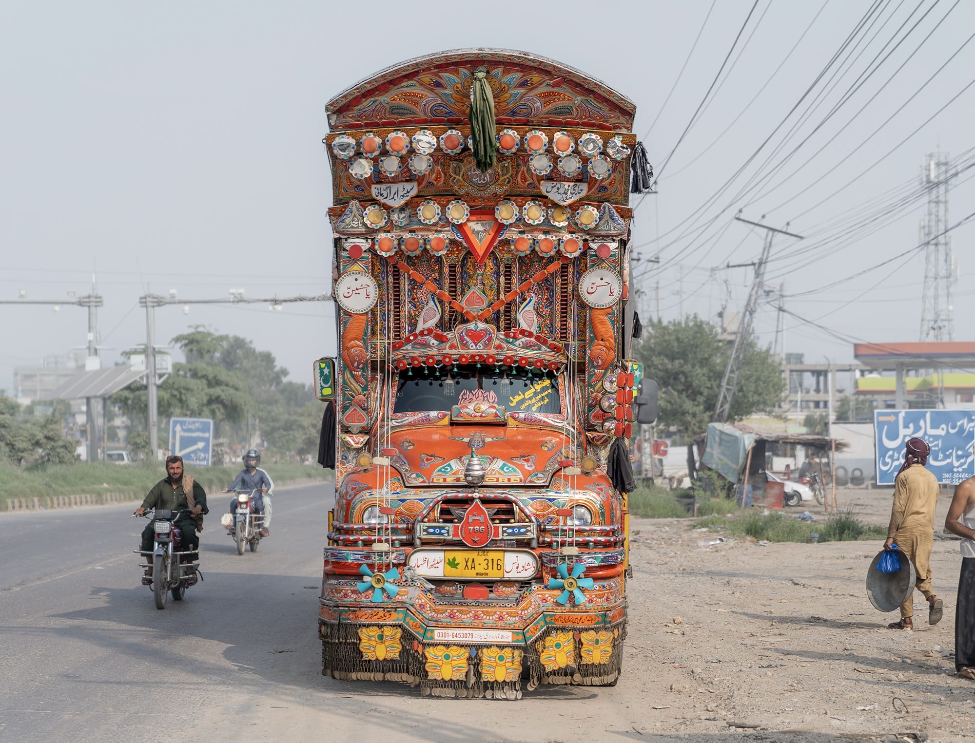 a colorfully painted truck painted with red and orange vibrant motifs and two motorcylists on the road next to