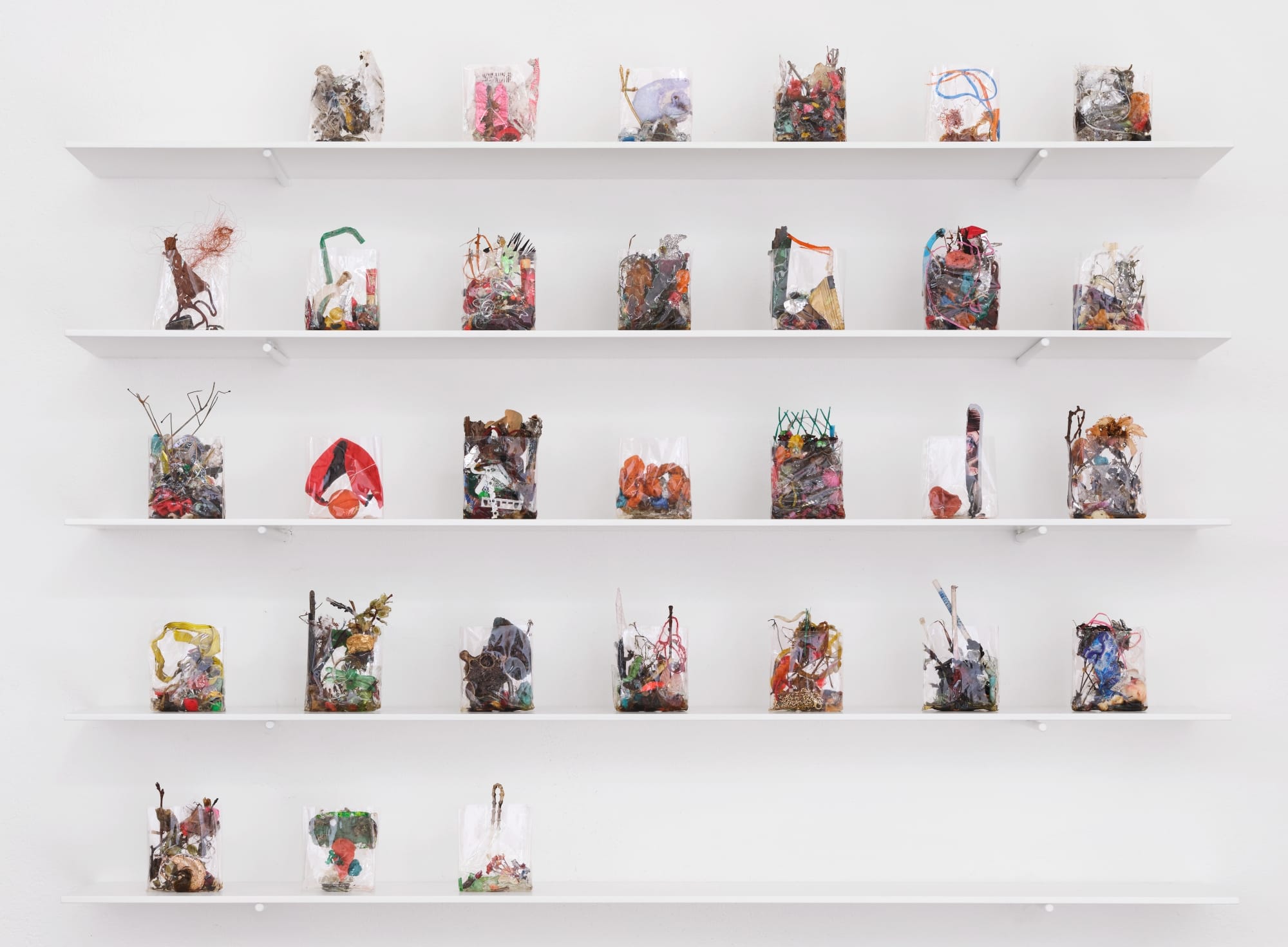 a collection of small ikebana-like sculptures in cellophane arranged like a month calendar on white shelves