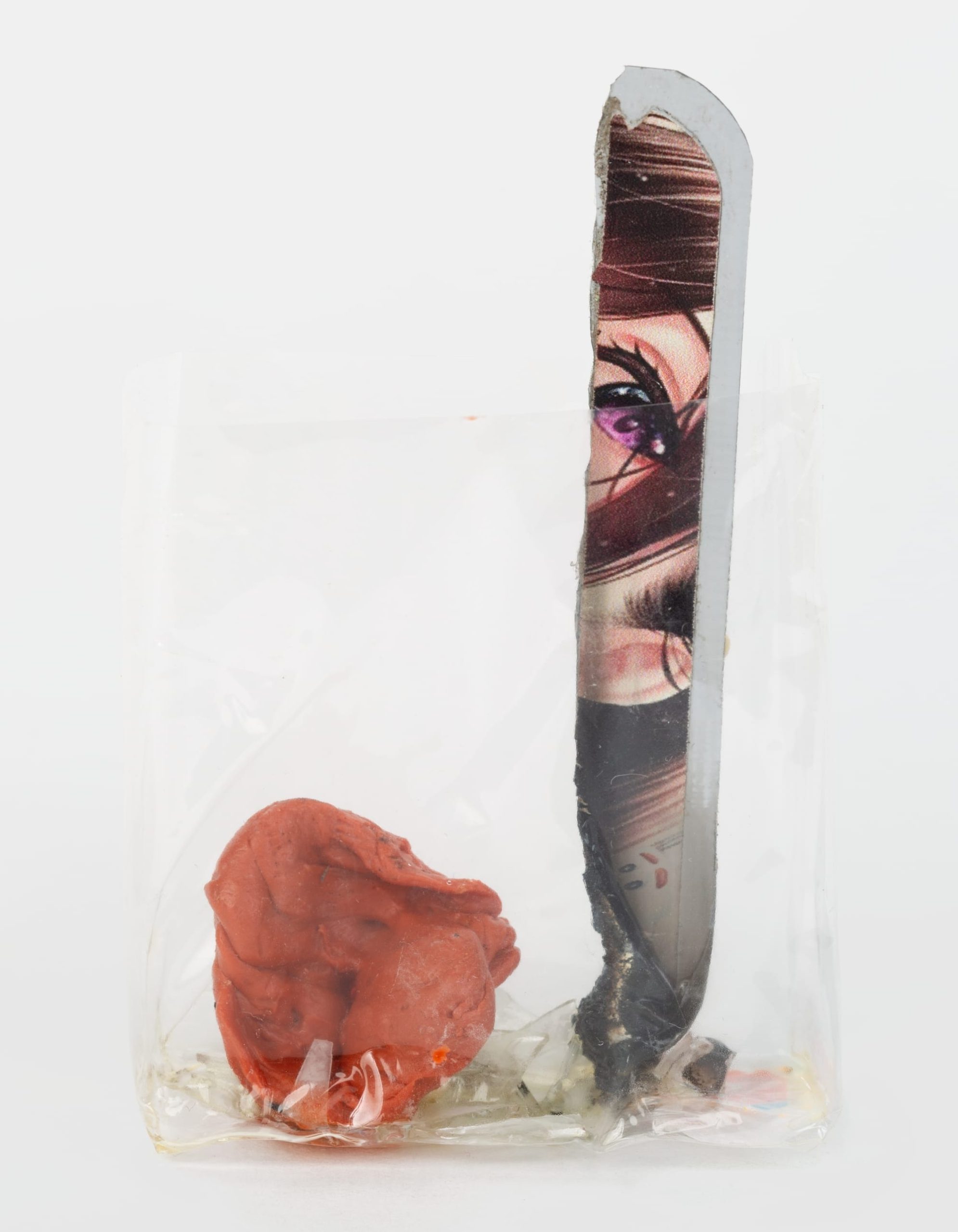 a scrap of paper with eyes, an orange substance, and other refuse in a clear plastic cellophane wrapper