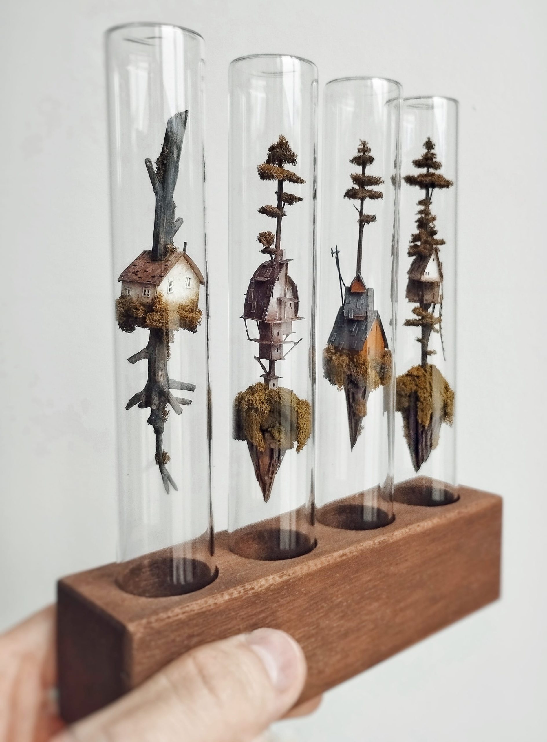 a sculpture by Michael Davydov of tiny houses and trees inside of glass vials