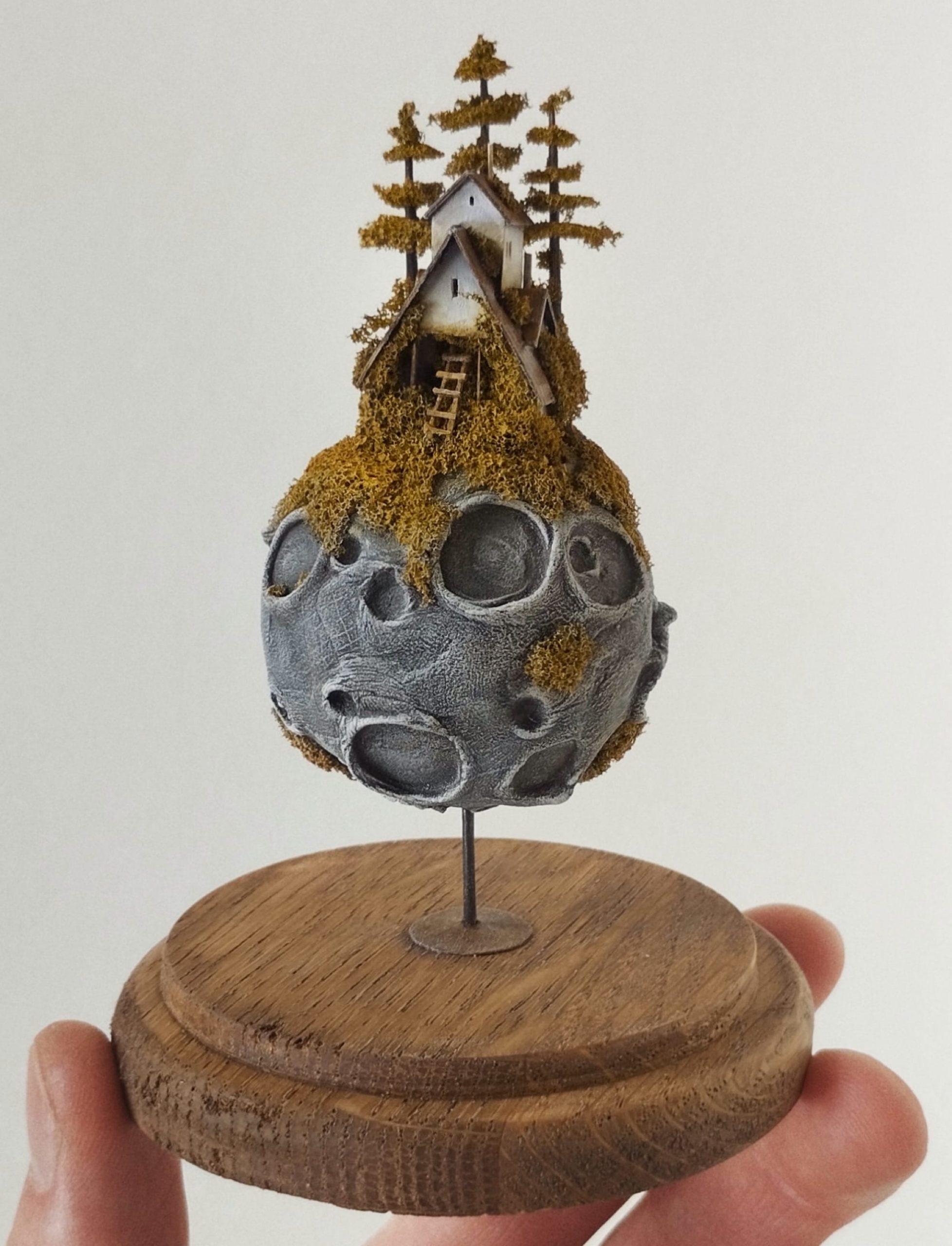 a miniature sculpture by Michael Davydov of a tiny house and trees on top of a moon-like rock