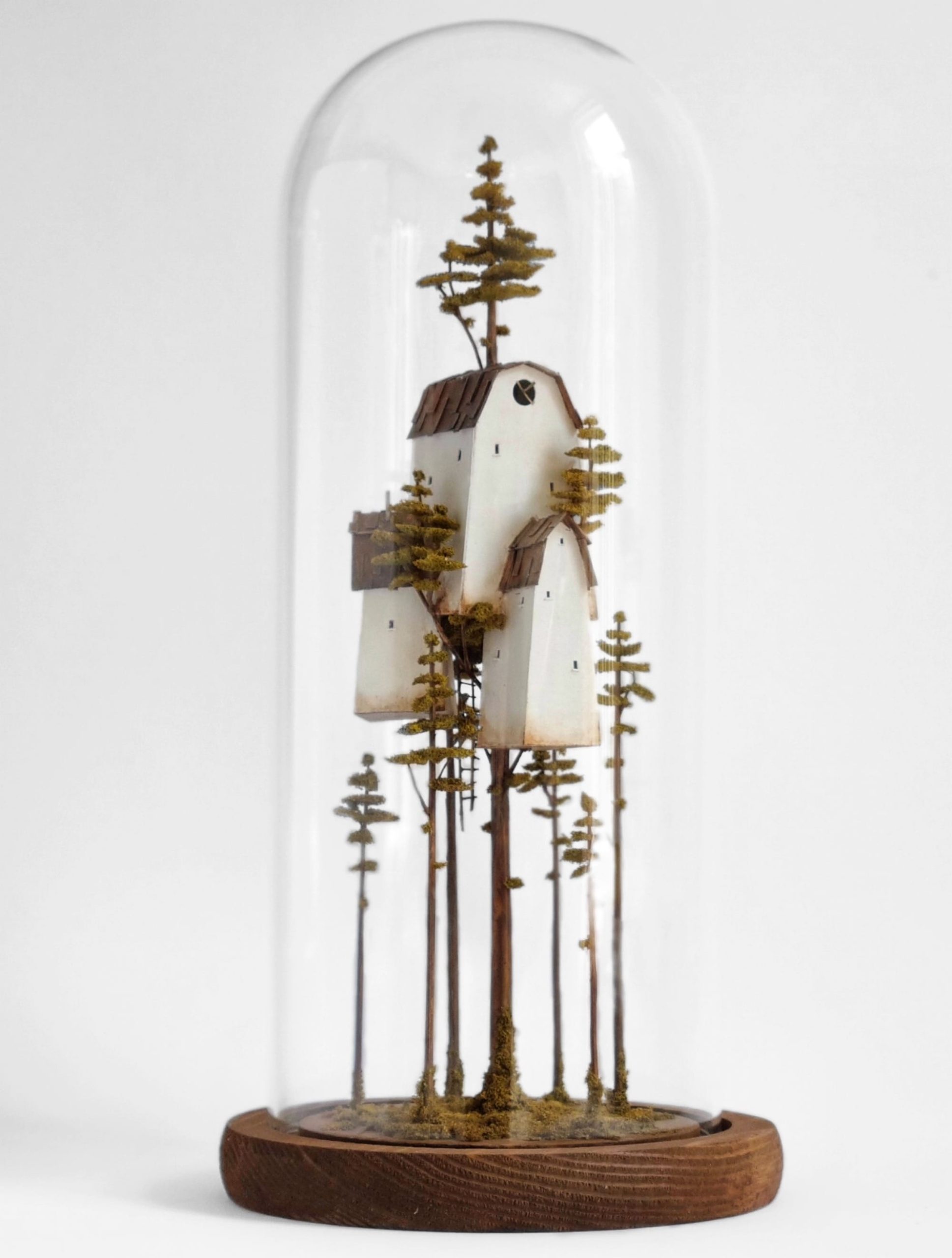 a miniature sculpture by Michael Davydov of a stack of tiny houses and trees inside of a glass dome