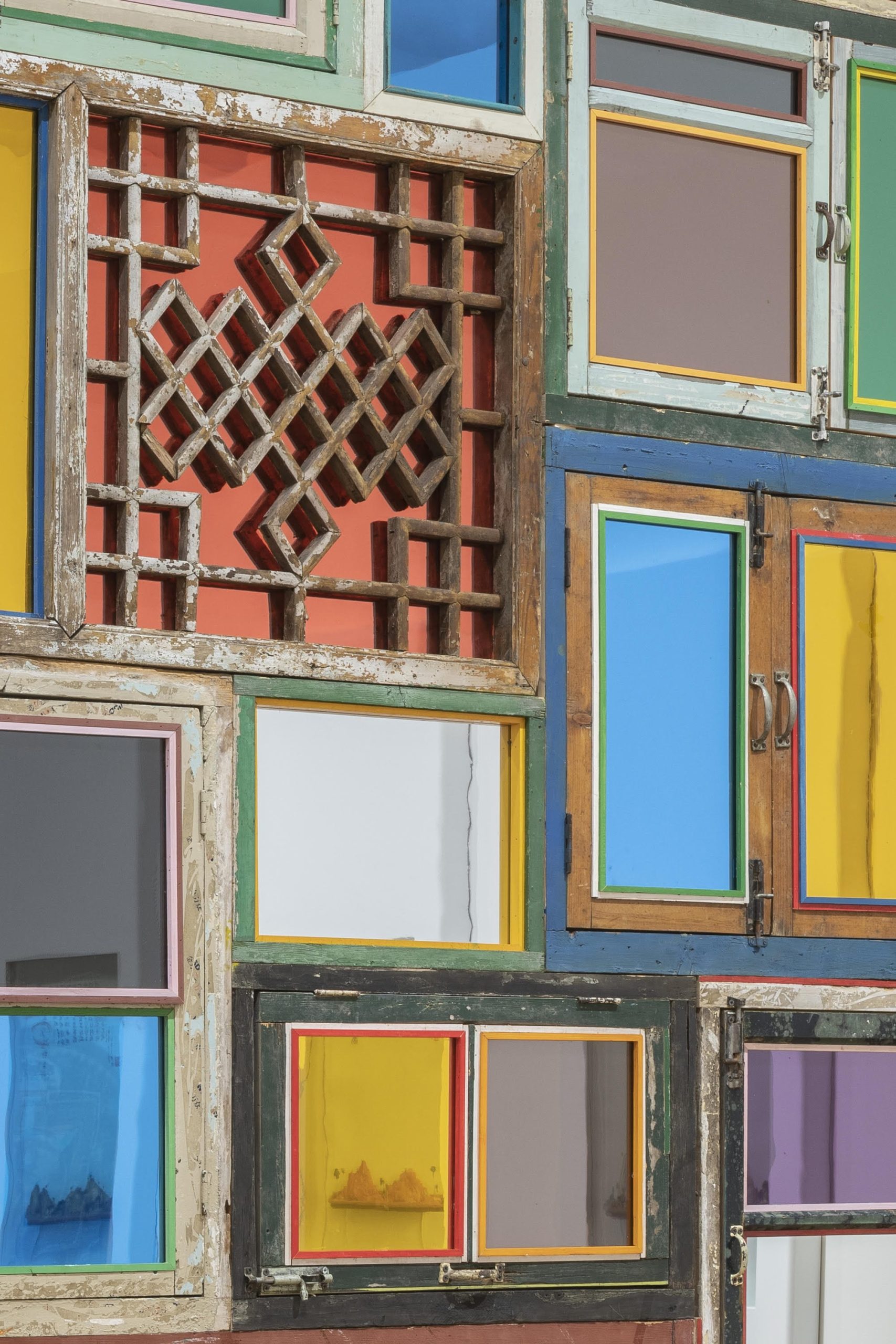 a detail of an installation by Song Dong using found wooden window frames and color-coated glass