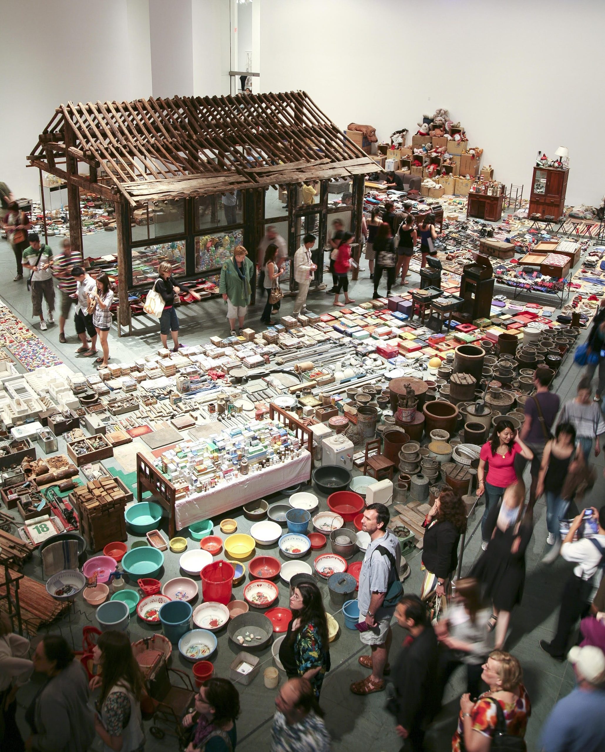 an overview of an exhibition and performance by Song Dong, showing thousands of items in a gallery space along with the structure of a small house