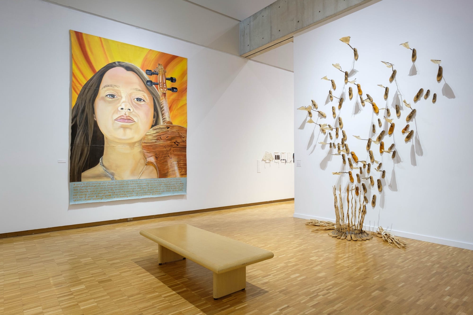 a large portrait of a woman with a violin and an installation of feet and corn husks by Raoul Deal in a gallery at the Haggerty Museum of Art