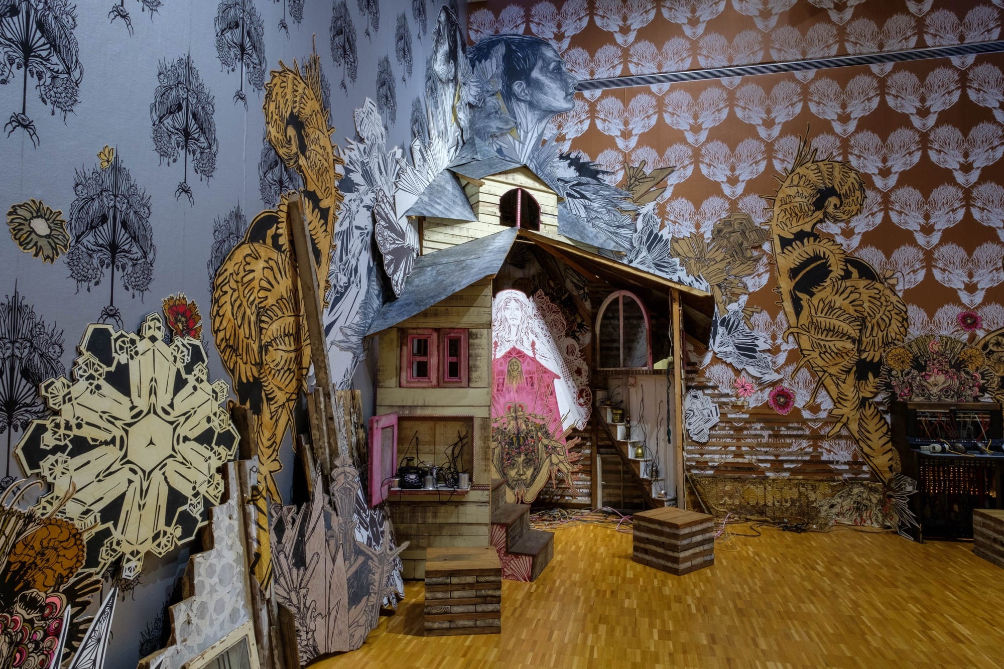 an installation by Swoon with patterned wallpaper, figures, vignettes, and a tarantula woman at the center. the piece is in a gallery at the Haggerty Museum of Art