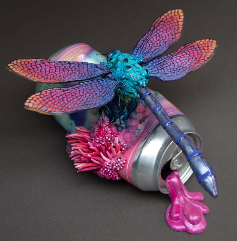 a sculpture by Stéphanie Kilgast of a multicolored dragonfly perched on an aluminum can