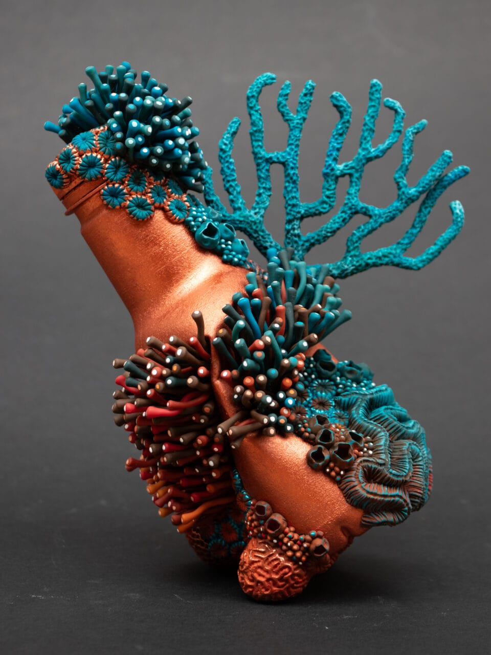 a sculpture by Stéphanie Kilgast of colorful coral growing around a coppy bottle