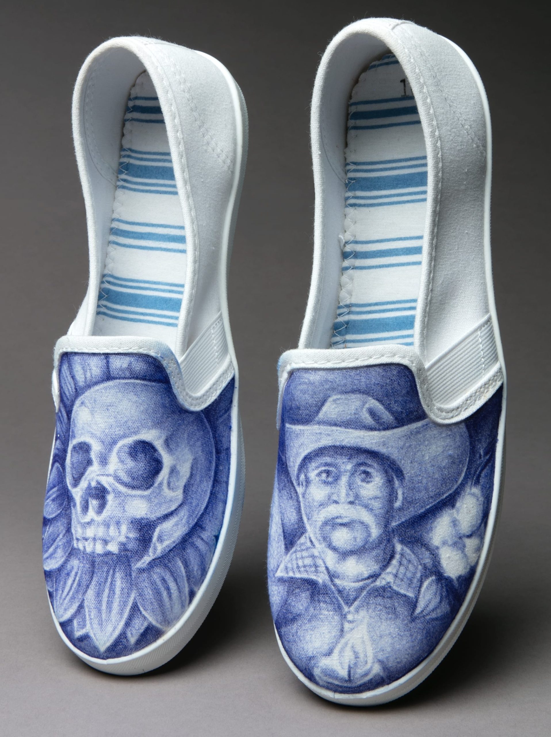 a pair of white shoes by John Paul Granillo with drawings of a skull and portrait of a laborer on the other