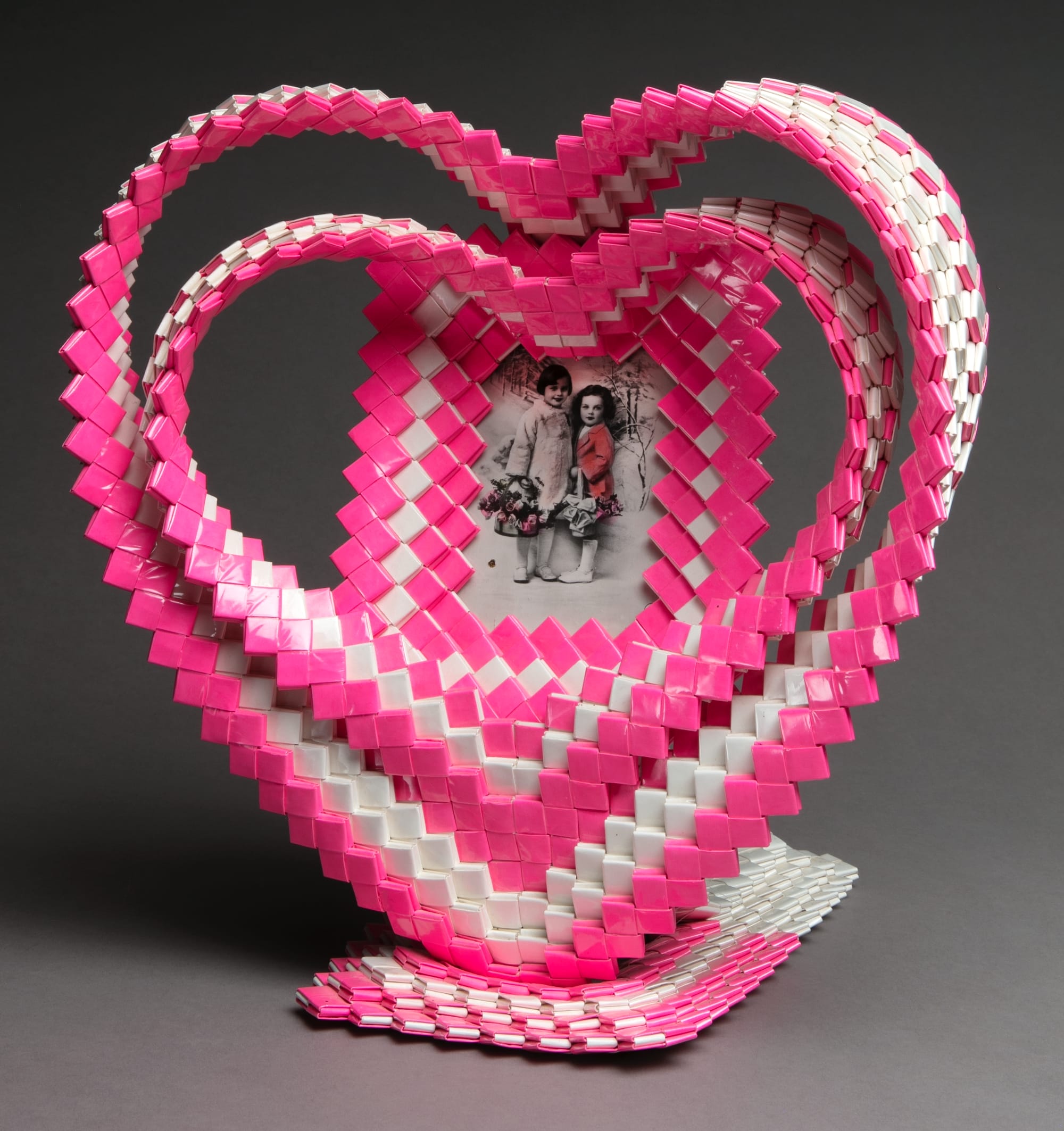 a frame make of pink and white gum wrappers in the shape of a heart with a family portrait at the center