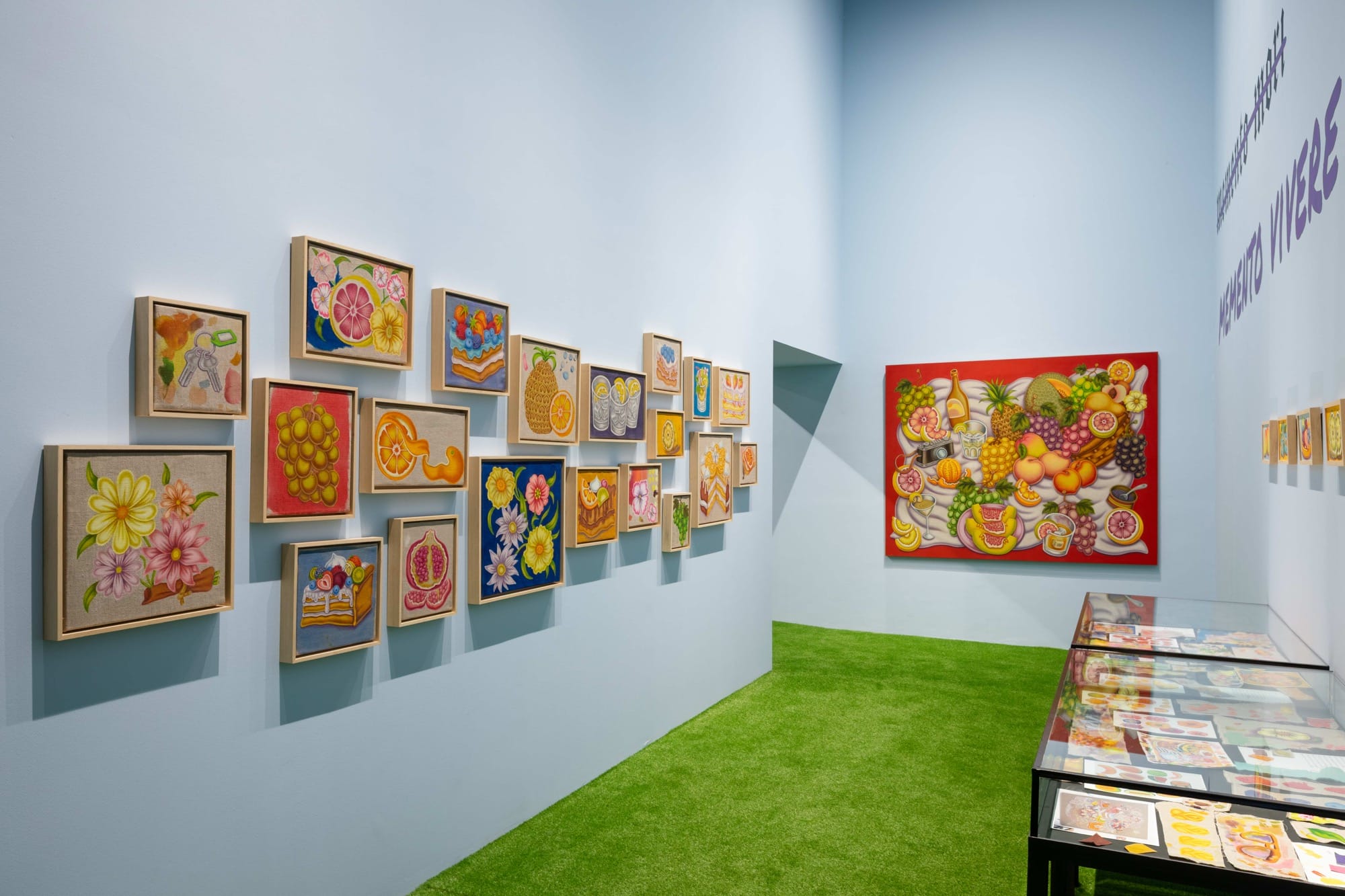 a number of small paintings by Pedro Pedro of numerous fruits and treats, installed salon-style on a white wall