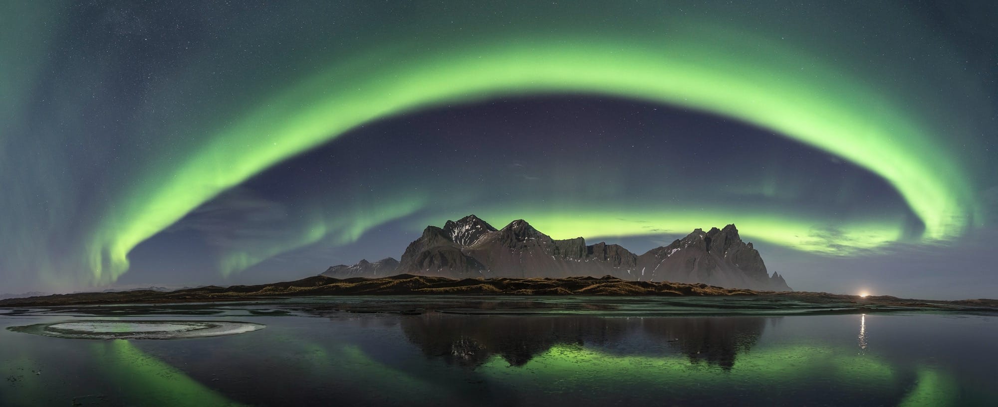 an arc of green aurora borealis over a northern landscape