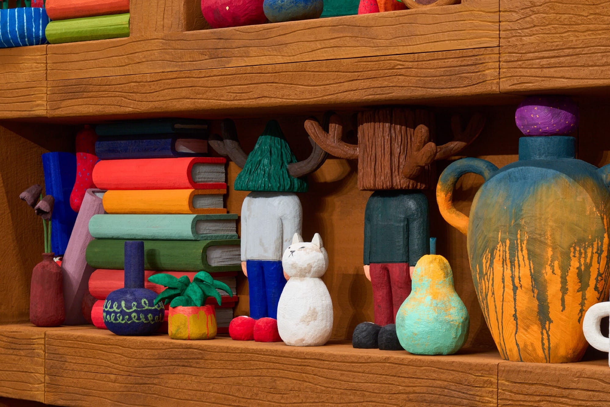 a close-up detail of a sculptural installation by Yuichi Hirako of an oversized shelf filled with cartoonish domestic forms like vases, food, candlesticks, and other objects